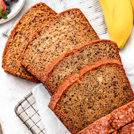 Banana bread recipe made with oil featuring a moist loaf sliced on a wooden board.