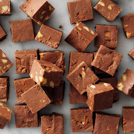 Fudge recipe featuring creamy chocolate fudge squares with chopped nuts on a white plate.