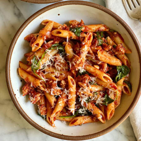 Pasta recipes featuring spaghetti with marinara sauce, garnished with fresh basil and Parmesan cheese on a white plate.