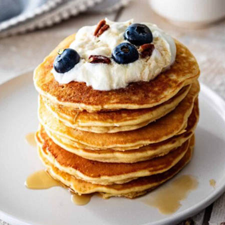 Sweet pancake recipe featuring fluffy pancakes stacked with syrup and fresh berries on top.