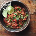 Bowl of fresh habanero salsa with cilantro and lime on a wooden table.