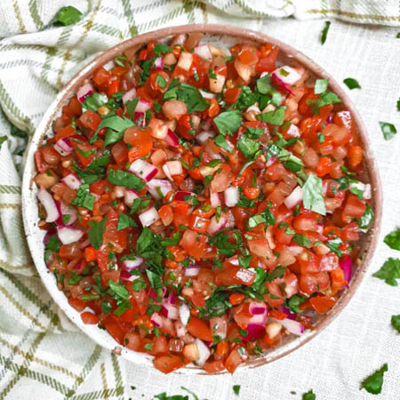 Salsa recipe featuring fresh tomatoes, onions, cilantro, and lime juice in a white bowl.