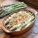 Golden asparagus casserole with breadcrumbs and cheese on a wooden table.