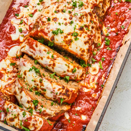 A freshly baked Italian meatloaf topped with marinara sauce and garnished with basil, served alongside roasted vegetables.