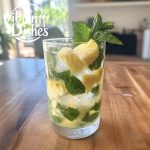 Pineapple mojito with mint, lime, and ice cubes on a wooden table.