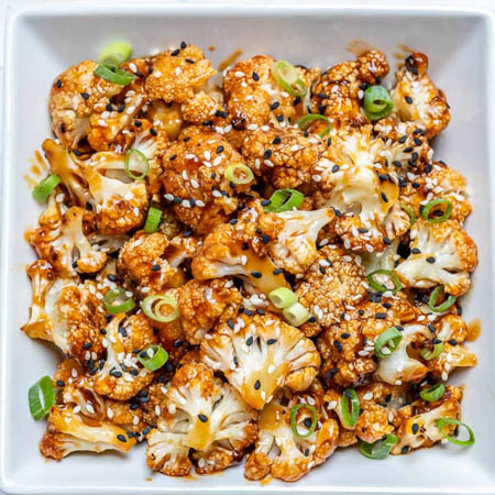 Cauliflower recipes featuring roasted cauliflower florets garnished with fresh herbs and Parmesan on a baking sheet.