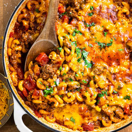 Simple goulash recipe with hamburger featuring pasta, tomato sauce, and melted cheddar cheese in a bowl.