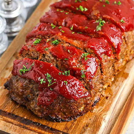 A perfectly smoked meatloaf served on a wooden platter, glazed with BBQ sauce and garnished with fresh parsley.