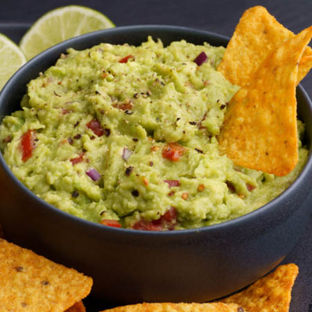 Spicy guacamole recipe featuring creamy avocado dip garnished with jalapeños, cilantro, and lime slices.