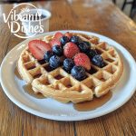 Golden Kodiak waffle recipe topped with blueberries, strawberries, and maple syrup on a white plate.